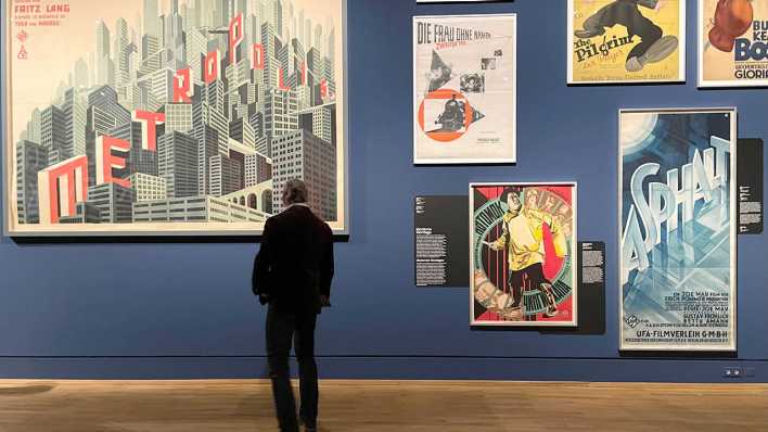Ein Mann schaut sich in einer Ausstellung historische Filmplakate an