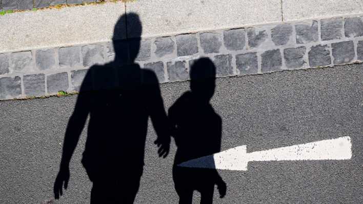 Der Schatten von einem Mann und einem Kind sind auf einer Straße mit einem Pfeil zu sehen.
