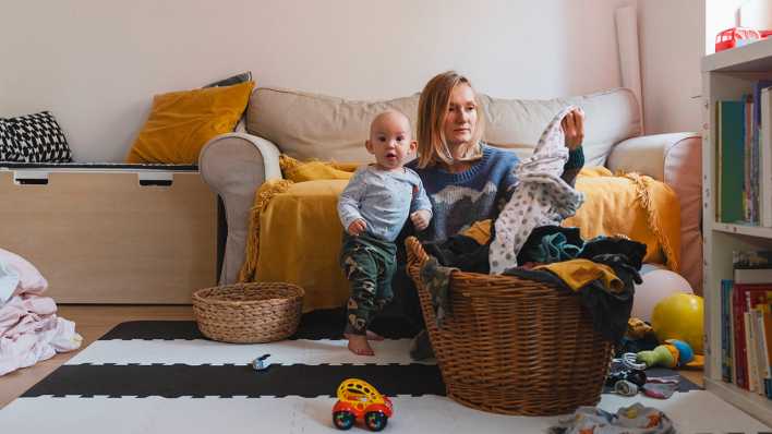 Eine Mutter sitzt im Wohnzimmer neben ihrem Sohn auf dem Fußboden und sortiert Wäsche.