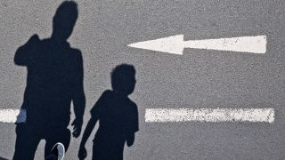 Symbolbild: Der Schatten von einem Mann und einem Kind sind auf einer Straße mit einem Pfeil zu sehen am 07.07.2023. (Quelle: dpa/Julian Stratenschulte)
