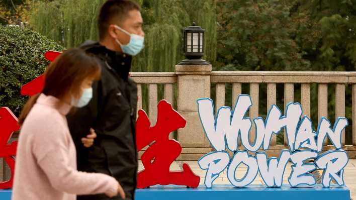 Chinesisches Paar geht in Wuhan an einem Schild "Wuhan Power" vorbei, das die Erholung von Covid19 feiert.