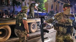 Mitglieder des Söldnergruppe Wagner bewachen einen Bereich, während andere ihren Panzer auf einen Lastwagen auf einer Straße in Rostow am Don laden, bevor sie einen Bereich im Hauptquartier des südlichen Militärbezirks verlassen.