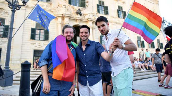 Drei Menschen schwenken Regenbogenfahnen in Maltas Hauptstadt Valletta (Bild: picture alliance / Photoshot)