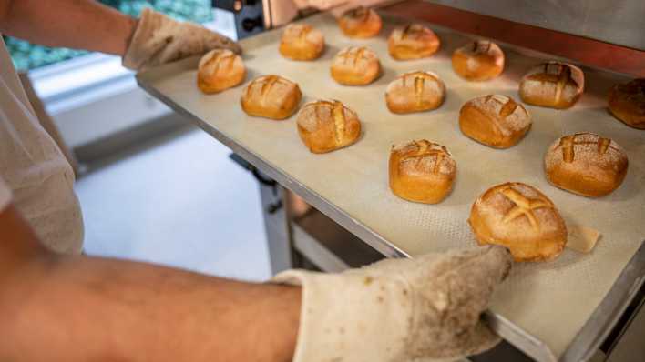 Eine Person schiebt in der Bäcker-Innung Berlin Blech mit Brötchen in den Ofen.