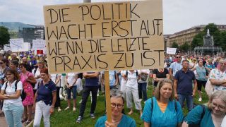 Eine Ärztin hält bei einer Demonstration ein Schild hoch mit der Aufschrift "Die Politik wacht erst auf, wenn die letzte Praxis zu ist".