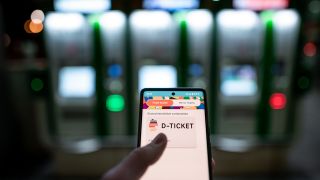 Ein Mann hält ein Mobiltelefon, auf dem das "D-Ticket" gekauft werden kann, vor Ticketautomaten am Hauptbahnhof Essen in der Hand.