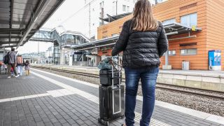 Frau mit Koffer wartet am Gleis auf einen Zug