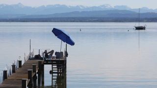 Menschen genießen unter einem Sonnenschirm auf einem Steg die sommerlichen Temperaturen am Ammersee