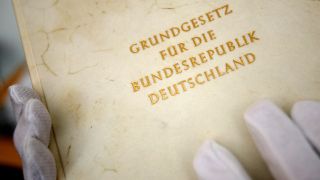 Eine Person hält die Urschrift des Grundgesetzes der Bundesrepublik Deutschland in den mit weißen Handschuhen überzogenen Händen.