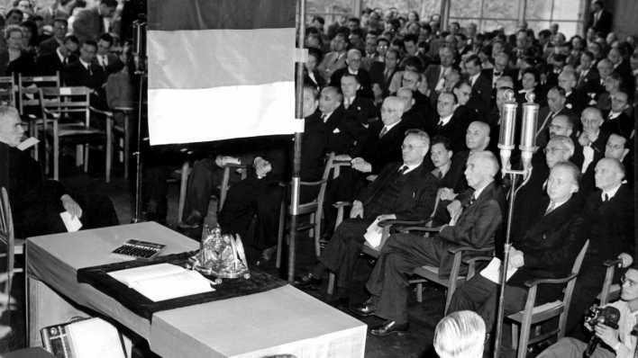 Unter einer schwarz-rot-goldenen Fahne liegt am 23.05.1949 das Grundgesetz der Bundesrepublik Deutschland