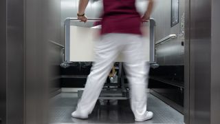 Eine Krankenpflegerin und ein Krankenpfleger schieben ein Krankenbett aus einen Aufzug eines Krankenhauses.