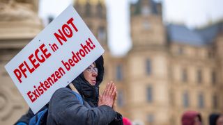 Bei einer Protestaktion hält eine Teilnehmerin ein Schild mit der Aufschrift "Pflege in Not - Existenzen bedroht!".