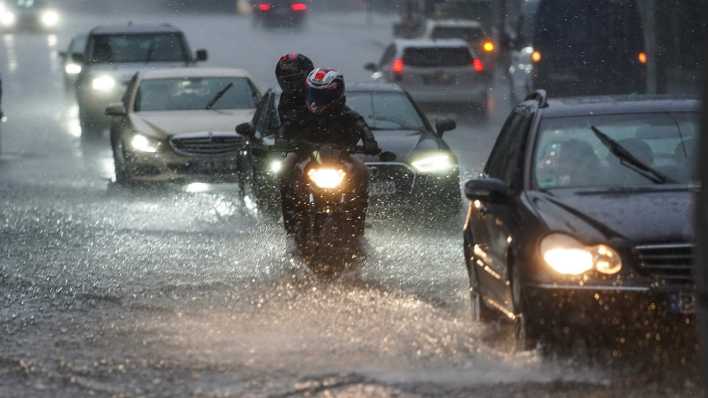 Autos und Motorräder fahren bei starkem Regen über die überflutete Friedrichstraße in Berlin-Mitte.