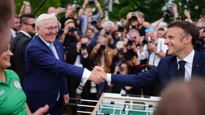 Emmanuel Macron, Präsident von Frankreich, besucht zusammen mit Bundespräsident Frank-Walter Steinmeier das Demokratiefest aus Anlass von 75 Jahren Grundgesetz und sie stehen dabei an einem Tischkicker.