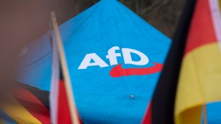 Das Logo der AfD ist bei einer Kundgebung in Düsseldorf neben Deutschlandflaggen auf einem Zeltpavillion zu sehen.