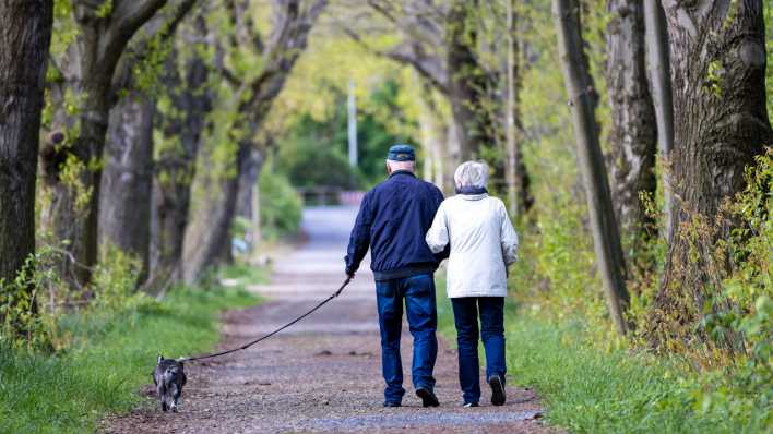 Eine Frau und ein Mann, beide im Rentenalter, gehen mit ihrem Hund spazieren.