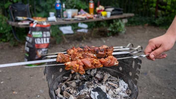 Ein Mann grillt im Volkspark Friedrichshain auf einem Grillplatz Fleischspieße.