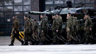 Soldaten marschieren vorbei an einem Leopard 2 A6 Kampfpanzer.