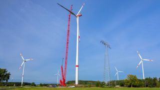 Ein Windrad wird auf einem Feld bei Drebkau in der Lausitz errichtet, mit einem Kran wird ein Rotorblatt montiert.