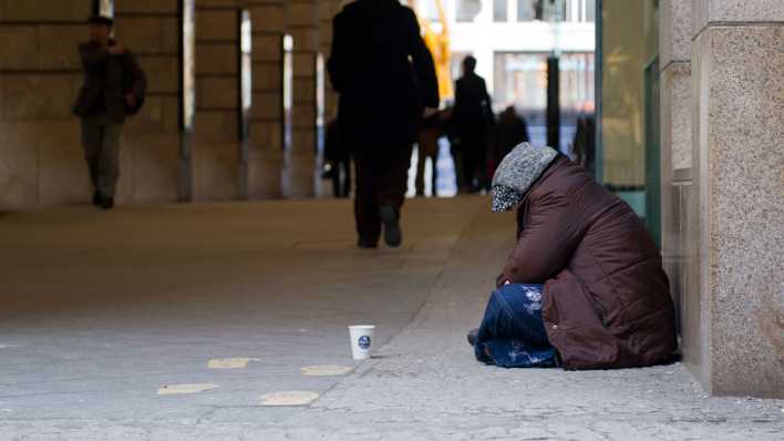 Eine Frau sitzt auf einem Gehweg in Berlin und bittet um Passanten um eine Geldspende (Bild: picture alliance/dpa/Franziska Gabbert)