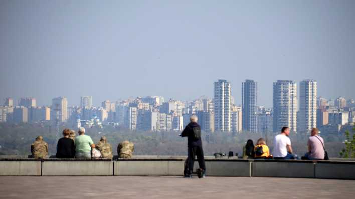 Am linken Ufer des Dnipro-Flusses sitzen Menschen auf einem Felsvorsprung gegenüber den Hochhäusern in der ukrainischen Hauptstadt Kiew.