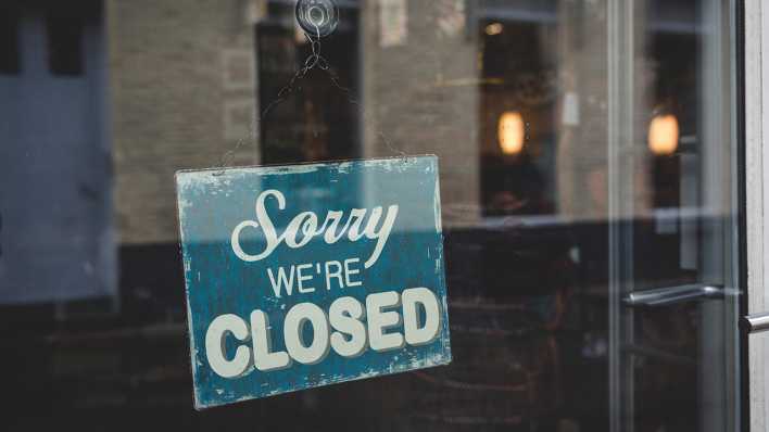 An einer Ladentür hängt ein Schild mit der Aufschrift "Sorry - we're closed".