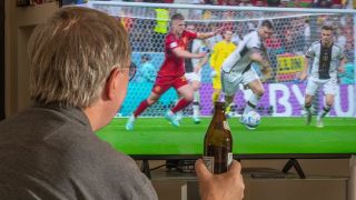Ein Fernsehzuschauer schaut mit einer Bierflasche in der Hand ein Fußballspiel der deutschen Nationalmannschaft.