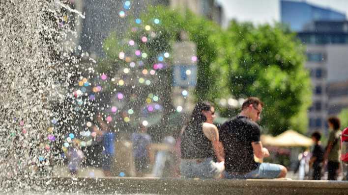 Zwei Menschen sitzen auf einem Brunnen an einem sommerlichen Tag.