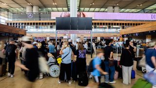 Nach einem IT-Problem warten viele Fluggäste am Hauptstadtflughafen BER vor einer schwarzen Anzeigetafel.