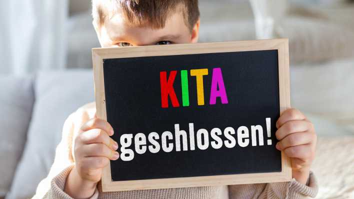 Junge hält ein Schild mit Aufschrift: Kita geschlossen! (Bild: picture alliance/CHROMORANGE/Michael Bihlmayer)