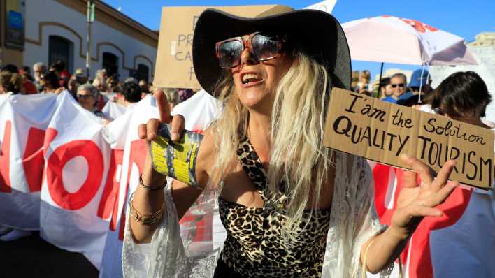 Eine Demonstrantin hält ein Schild hoch mit der Aufschrift "I am the Solution - Quality Tourism" bei einer Demonstration gegen den Massentourismus auf Mallorca.