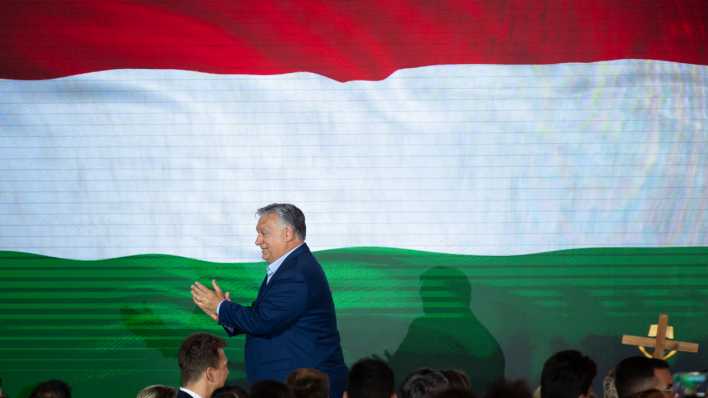 Der ungarische Ministerpräsident Viktor Orban klatscht vor einer Ungarnfahne (Bild: Denes Erdos/AP/dpa)