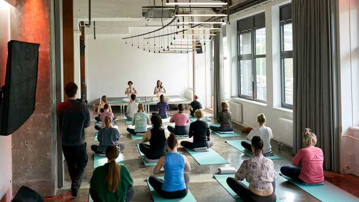 Frauen und Männer sitzen bei einem Yogakurs in Berlin auf Matten (Bild: picture alliance/Eventpress Radke)