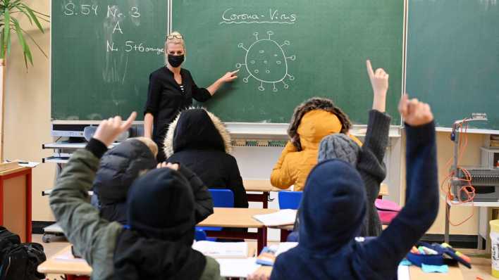 Eine Lehrerin mit Maske vor Schülern in Winterjacke im Klassenraum