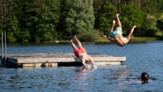 Jugendliche springen von einer Schwimminsel in einen See (Bild: picture alliance/dpa/Daniel Karmann)