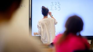 Eine Lehrerin schreibt eine Mathematikaufgabe auf eine digitale Schultafel