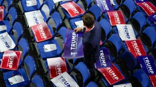 Ein Mann legt beim Parteitag der Republikaner "Trump"-Pappen auf Stühle (Bild: picture alliance / AP | Matt Rourke)