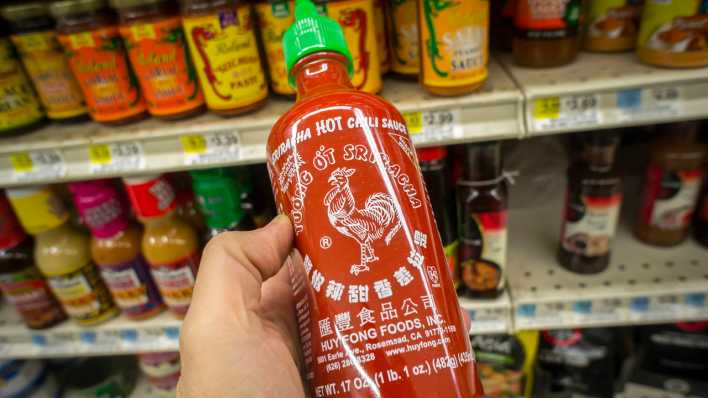 Mann in einem Supermarkt hält eine Flasche Sriracha-Sauce in der Hand