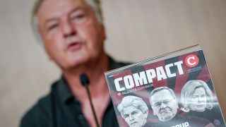 Jürgen Elsässer, "Compact"-Chefredakteur, gibt eine Pressekonferenz zur Aufhebung des Verbots der Zeitschrift durch das Bundesverwaltungsgerichts hinter einem Titelbild seines Magazins.