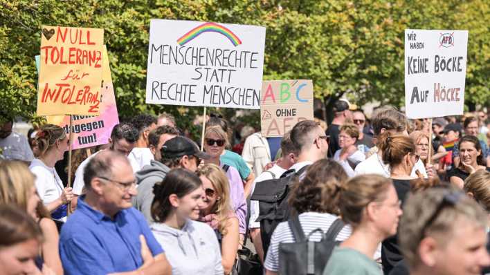 Demonstranten halten mehrere Schilder hoch, unter anderem mit der Aufschrift "Menschenrechte statt Rechte Menschen".