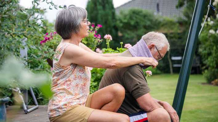 Hitzeschutz: Frau kühlt Nacken ihres Mannes im Garten (Bild: picture alliance/dpa-tmn/Benjamin Nolte)