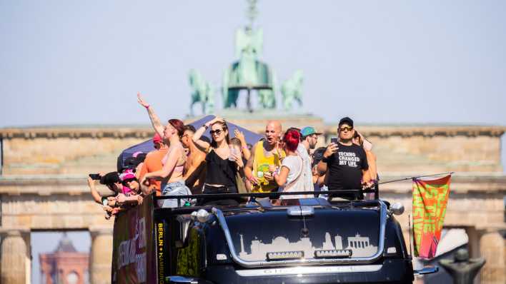 Menschen feiern bei der Technoparade "Rave the Planet" auf einem Wagen vor der Quadriga des Brandenburger Tors.