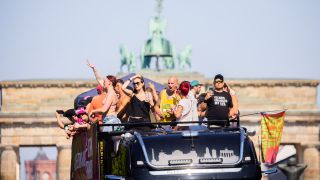 Menschen feiern bei der Technoparade "Rave the Planet" auf einem Wagen vor der Quadriga des Brandenburger Tors.