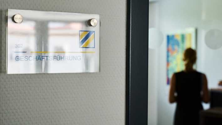 Symbolfoto: Eine Frau steht in einem Büro, an dessen Tür das Schild "Geschäftsführung" steht.