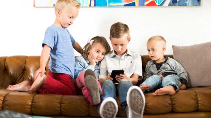 Vier Kinder sitzen auf einer Couch und schauen auf ein Smartphone (Bild: picture alliance / Bildagentur-online/Tetra Images)