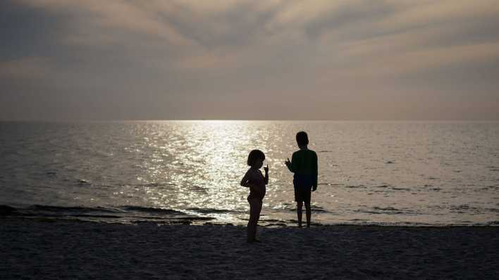 Geschwister stehen im Gegenlicht der untergehenden Sonne am Strand