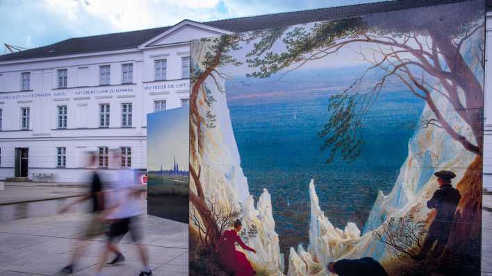 Passanten gehen an großformatigen Kopien von Gemälden von Caspar David Friedrich vor dem Pommerschen Landesmuseum in Greifswald vorbei. (Bild: picture alliance/dpa/Jens Büttner)