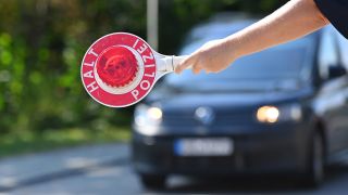 Ein Polizist hält eine Kelle mit der Aufschrift "Halt Polizei" vor ein Auto.