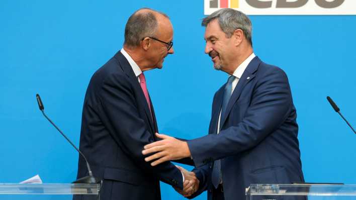 Friedrich Merz und Markus Söder schütteln einander die Hand auf einer Pressekonferenz.