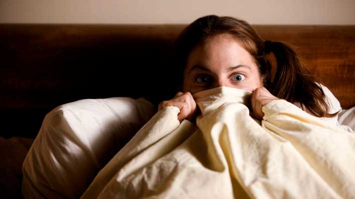 Frau im Bett zieht sich die Decke übers Gesicht